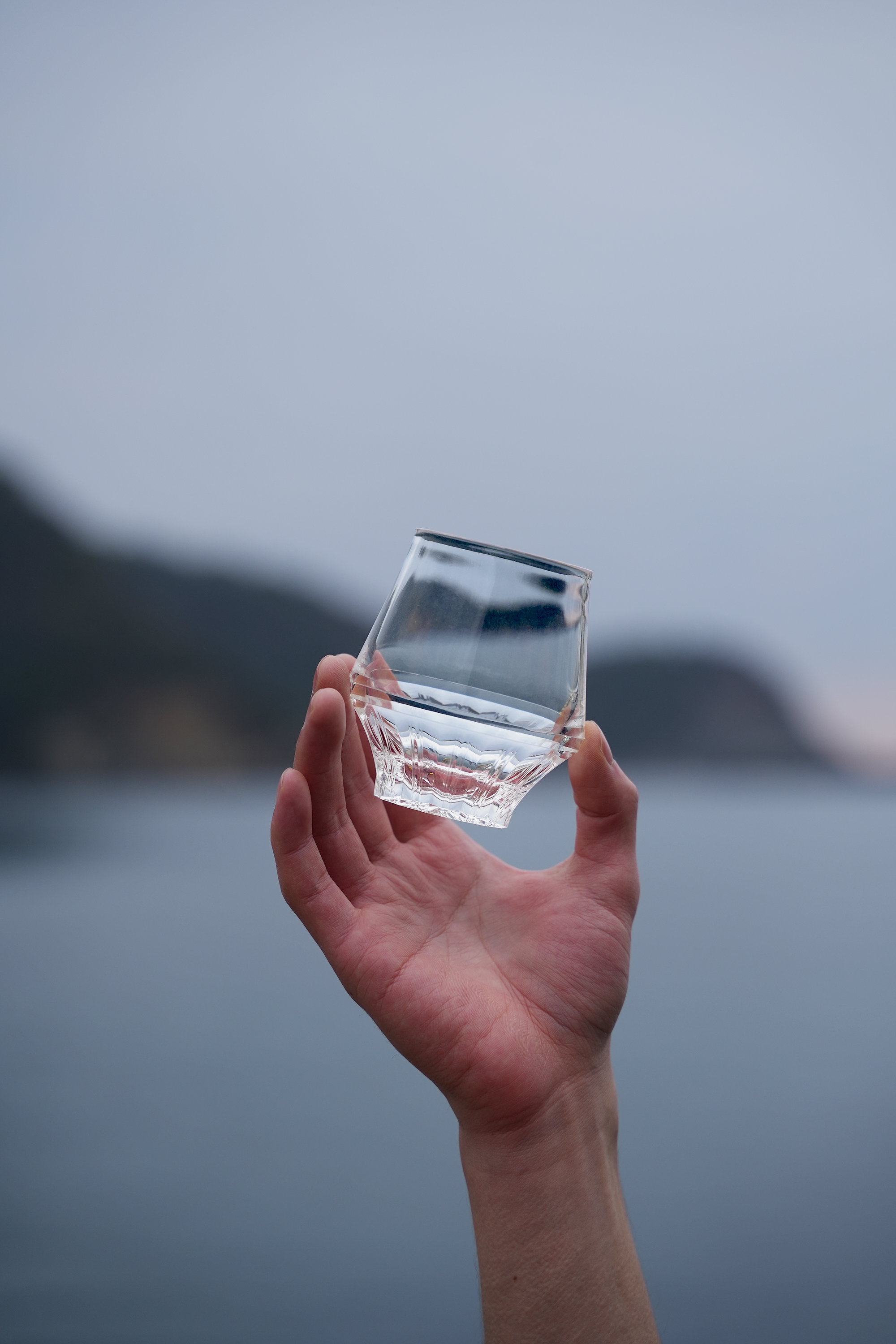【新商品】サステナブルでデザイン性に富んだ“割れないグラス”４月15日より一般販売開始のサブ画像2_画像の説明：海を背景にKINJO JAPAN F0（通称：SAKEグラス）を掲げているカット